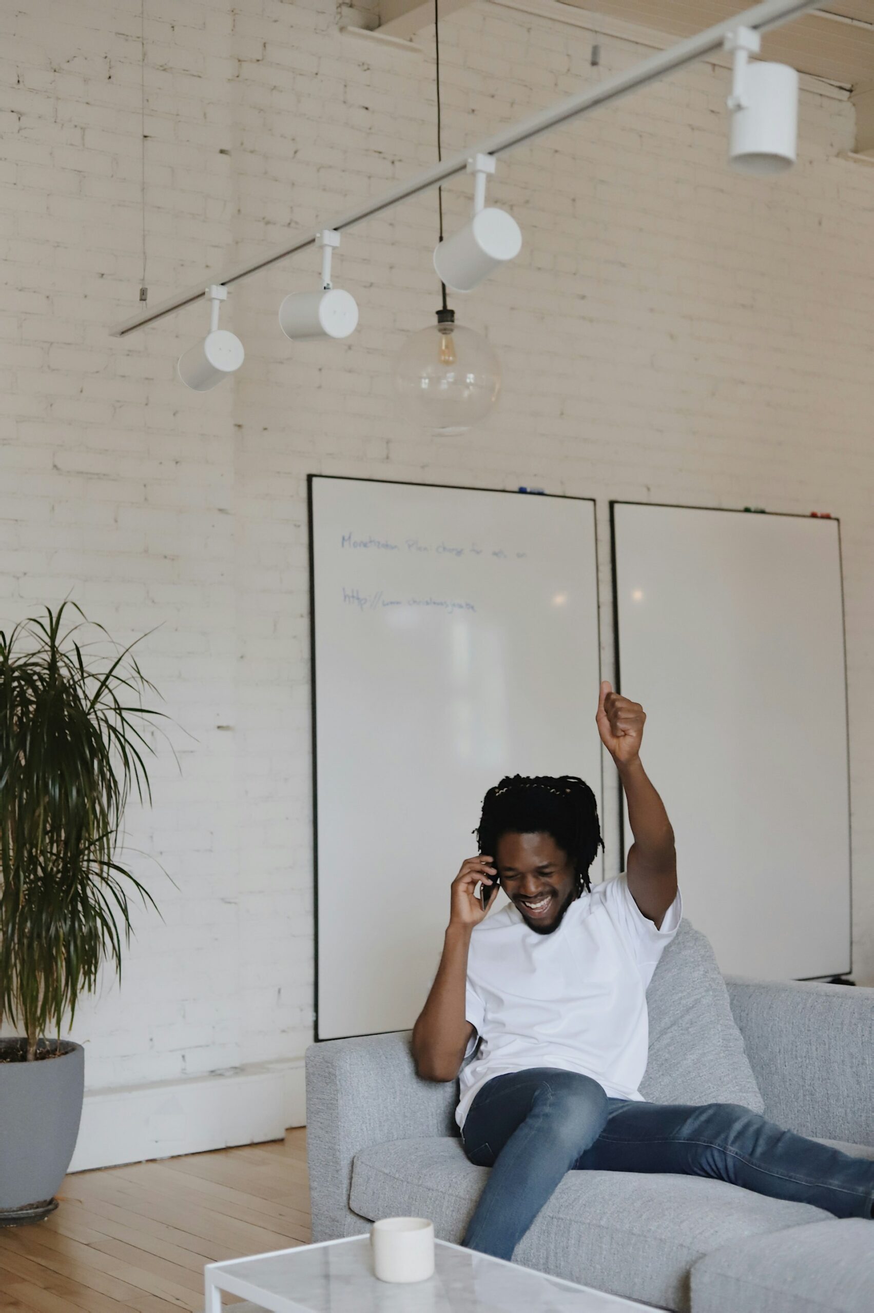 A black man in a white shirt celebrating while sitting on a coach.