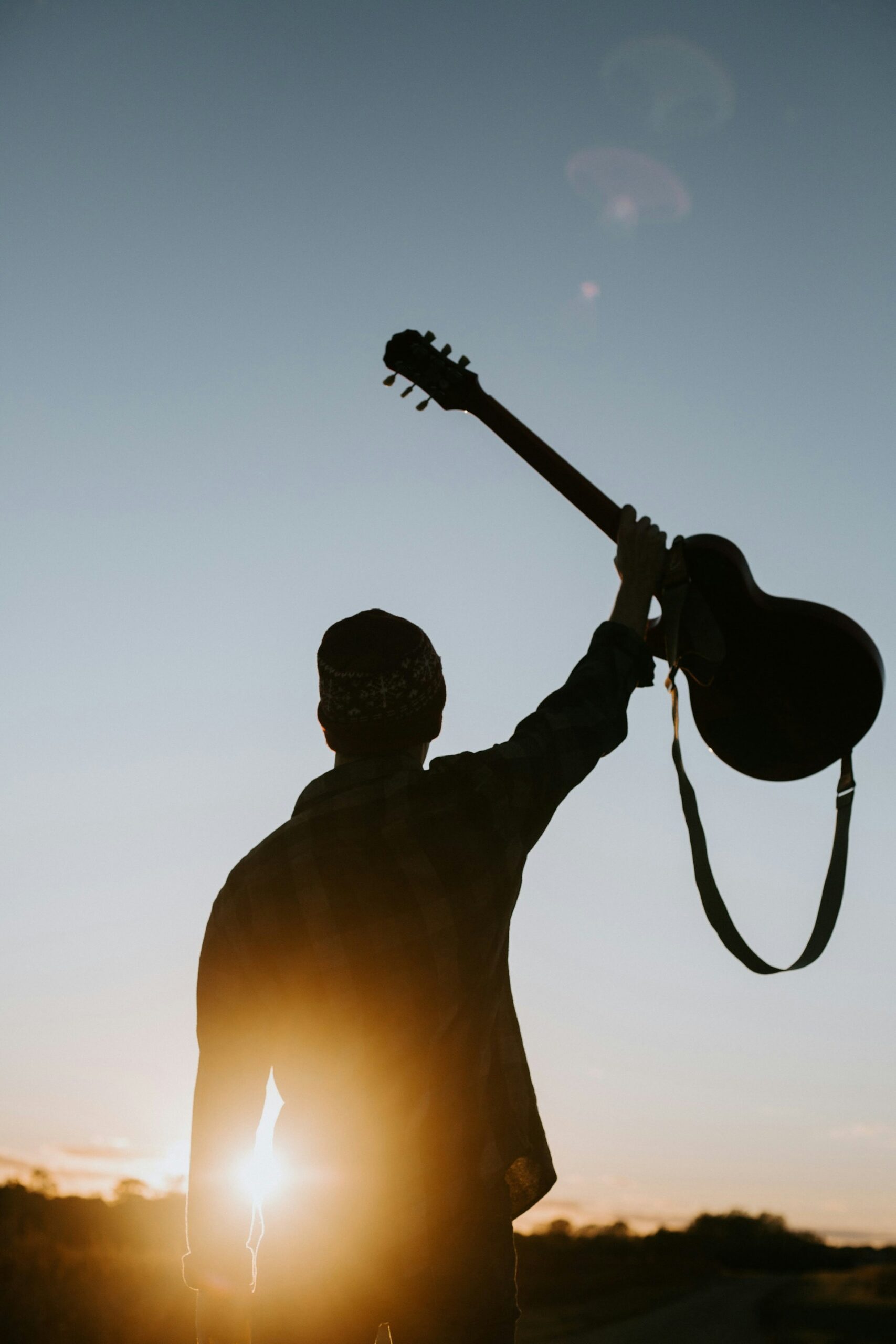 Silhouette of a man holding up a guitar in front of a sunset.