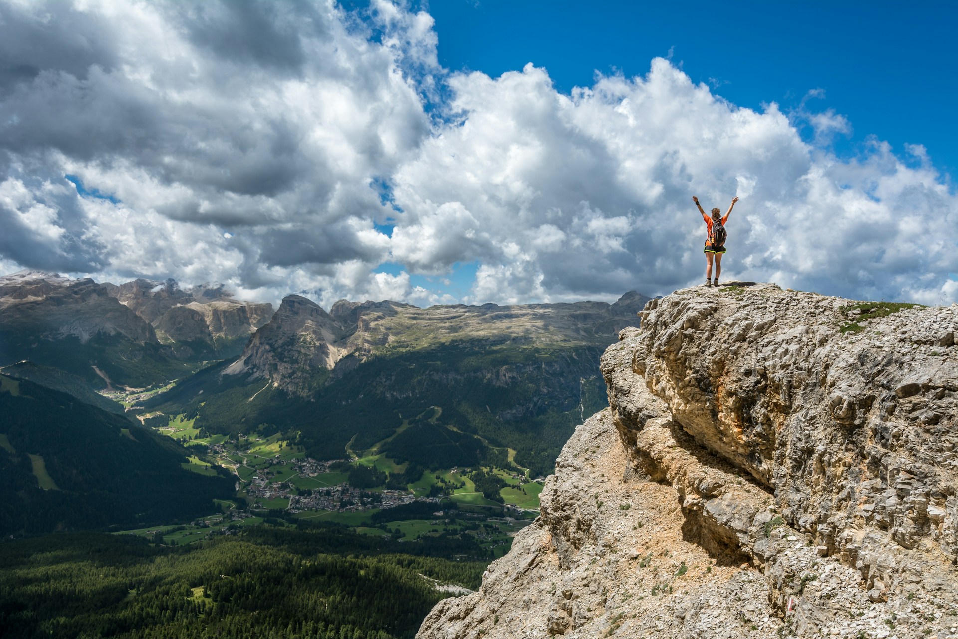 Person standing on top of a cliff in front of a valley with arms in the arm in celebration.